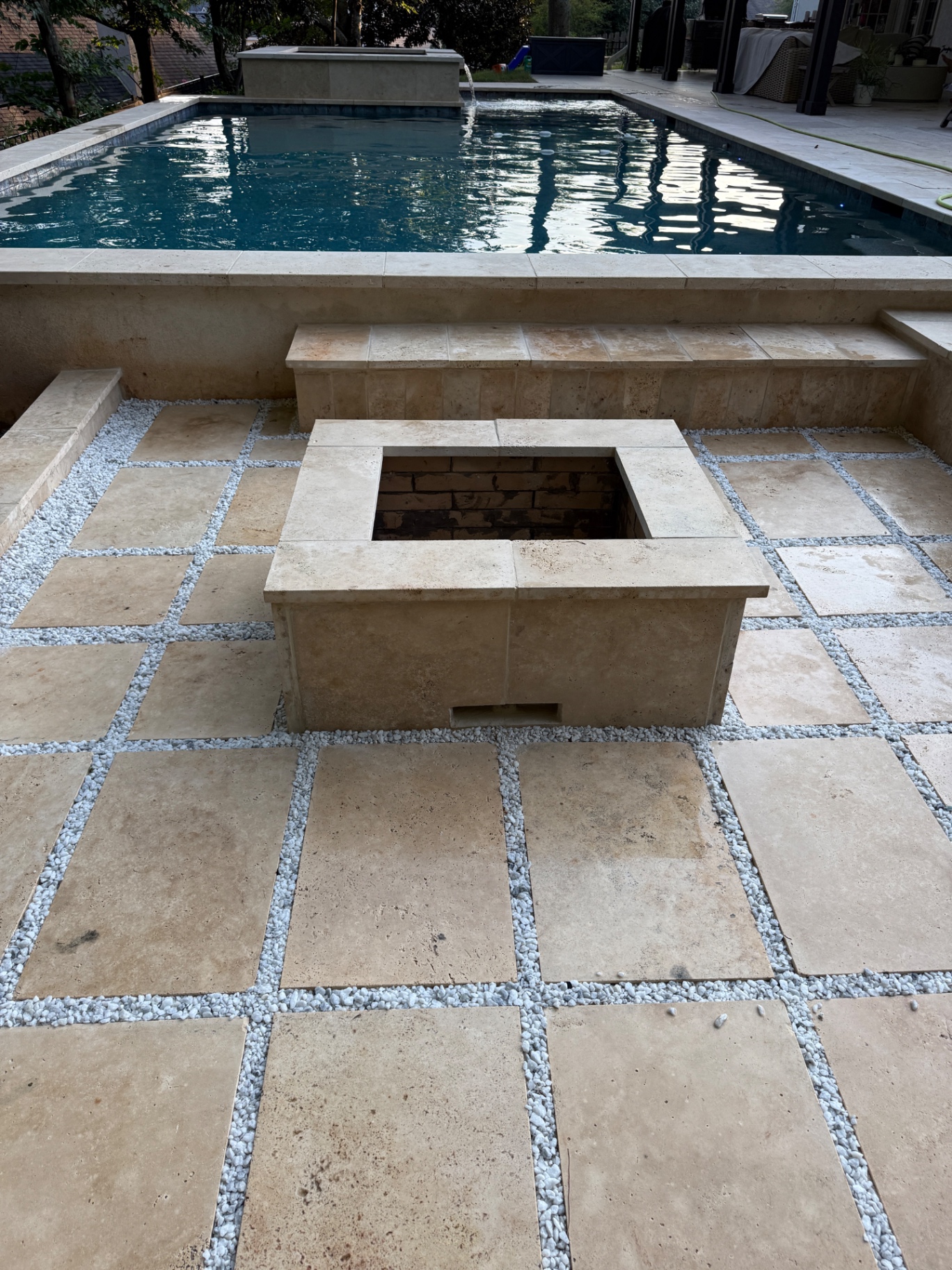 Travertine pool deck with a square stone fire pit and built-in benches