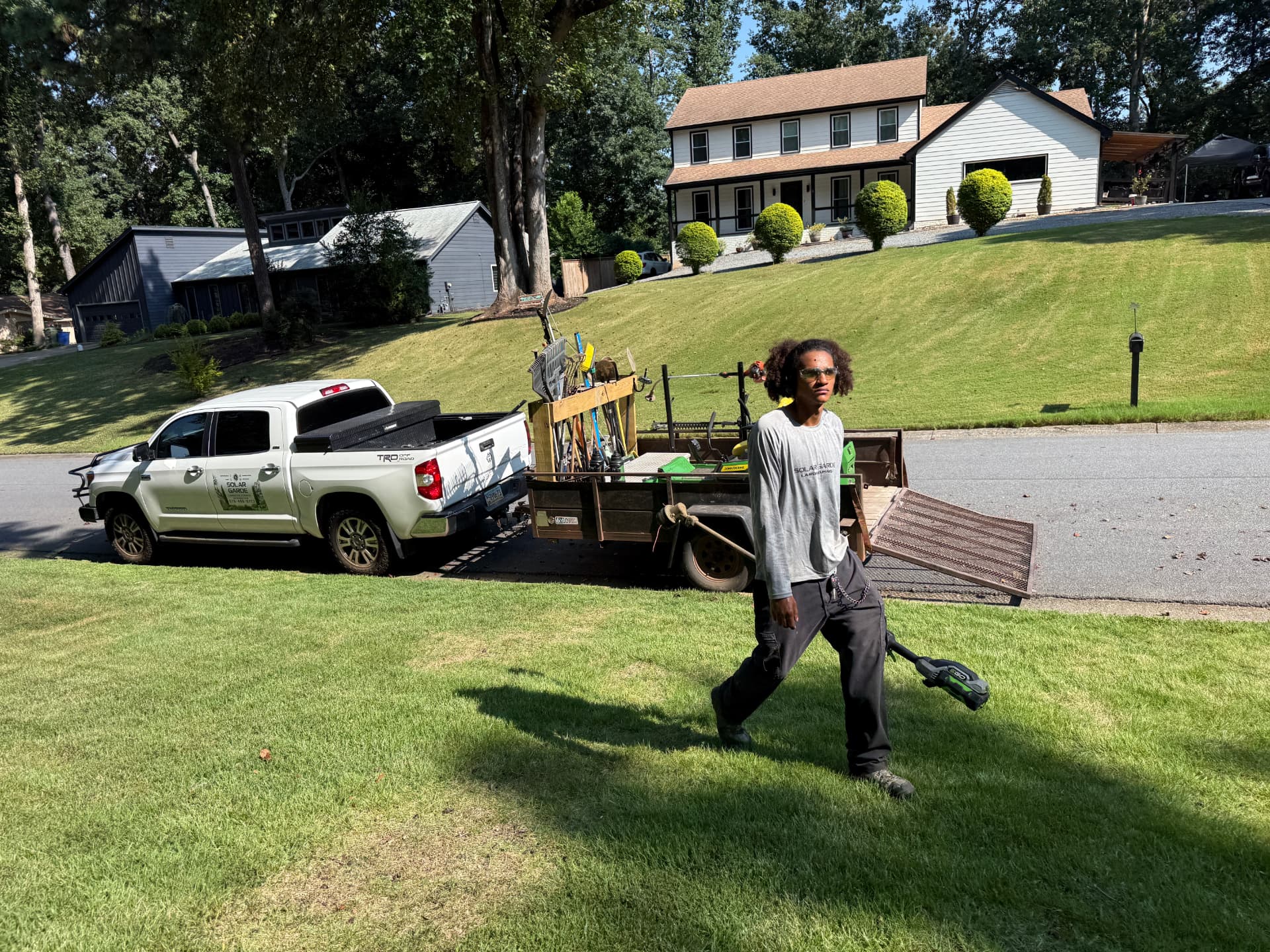 Solar Garde crew member edging a freshly mowed lawn in front of a Georgia home, branded truck and equipment trailer at the curb